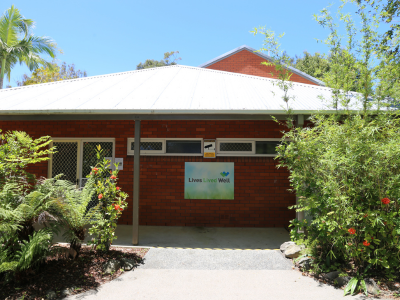 The front of the residential rehab centre: a one story brick building surrounded by trees and plants.